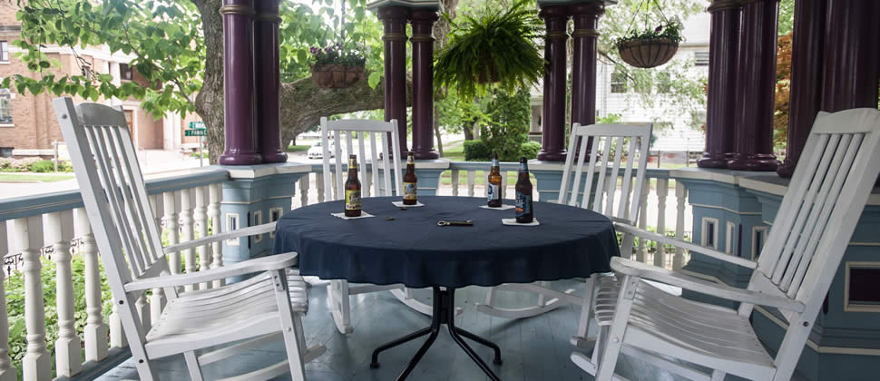 Table on the porch with 4 white rocking chairs, and 4 bottles of beer sitting on table
