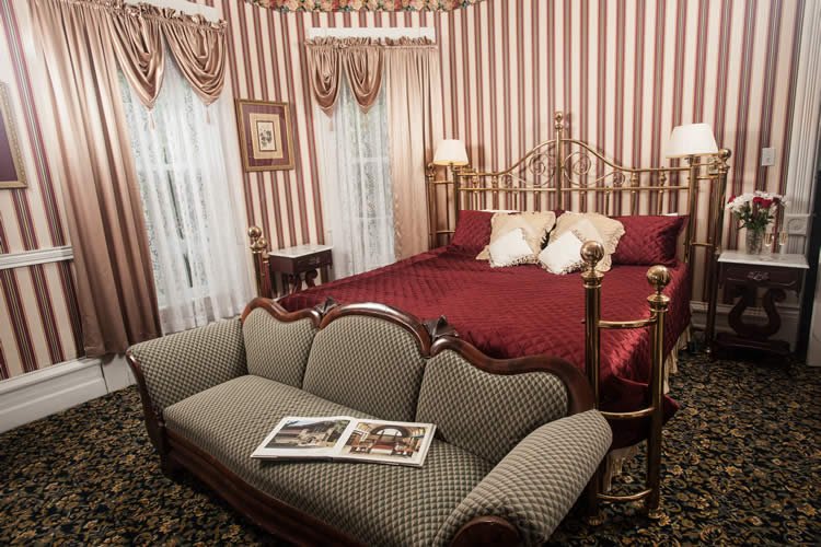 Brass king bed frame, burgundy bedspread with striped wall paper, with loveseat at the bottom bed