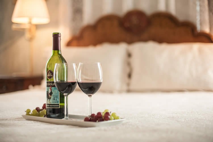 Wine bottle with two wine glass with red wine on a tray on the bed