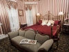 Brass king bed frame, burgundy bedspread with striped wall paper, with loveseat at the bottom bed